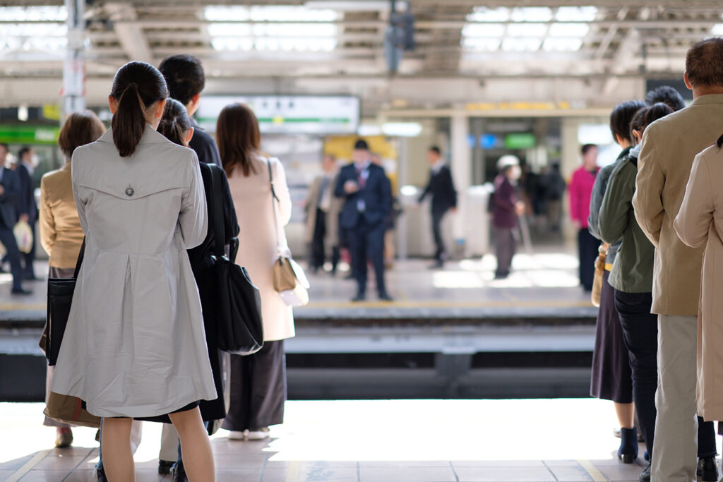 Japanese people queuing, waiting for their commuter train in a busy railway station in Tokyo on a bright spring day.